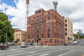 A multi-story building with a prominent red brick facade, a sign reading "Mantra," and a corner location with a street intersection. - Mantra One Sandy Bay Road (Hobart)