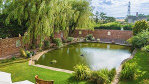 Um jardim tranquilo com lago, paredes de tijolo e um banco.