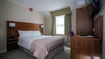 Una habitación de hotel con una cama grande, cabecera de madera, mesitas de noche con lámparas, un televisor montado en la pared y una ventana con cortinas.