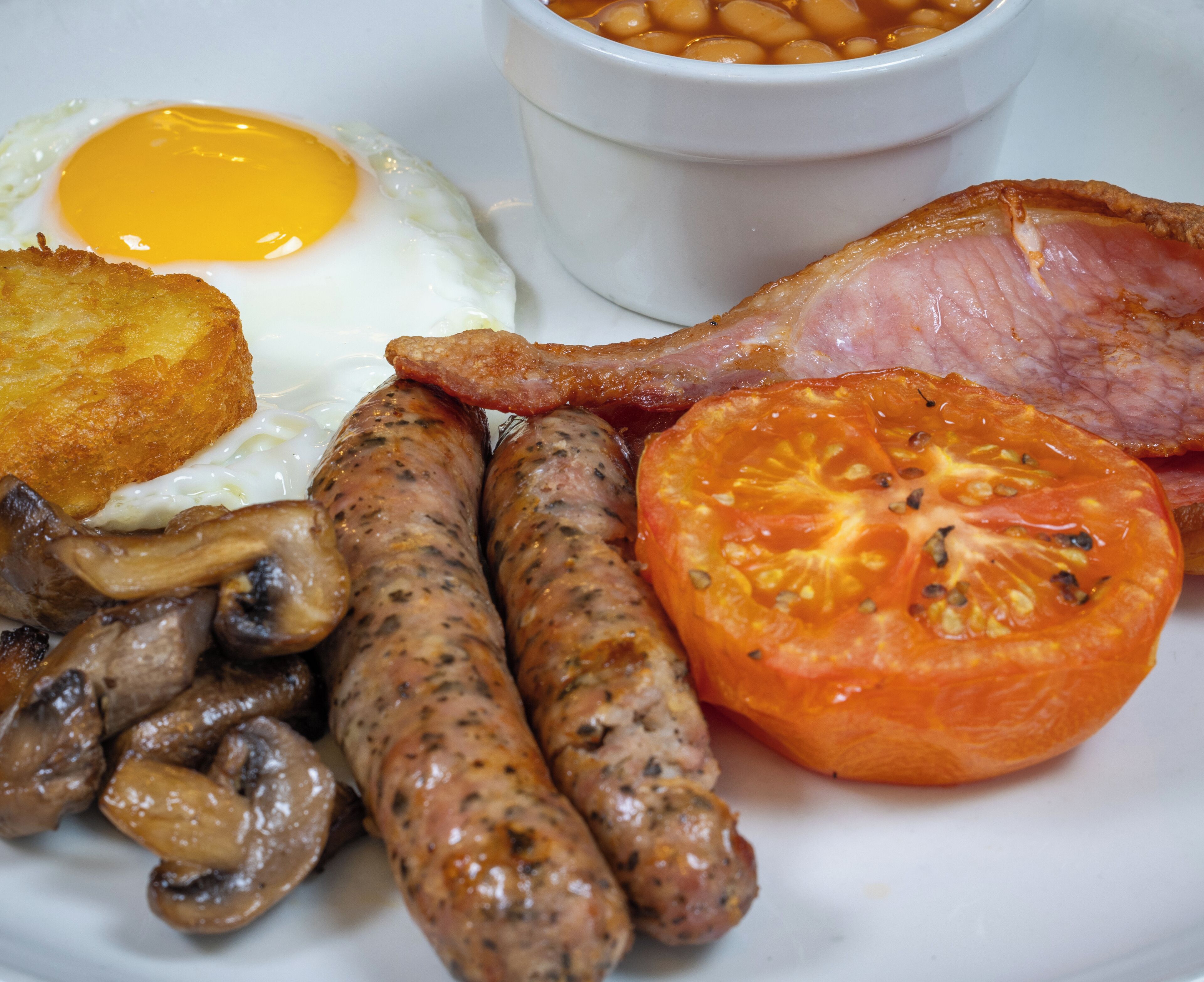A breakfast plate with eggs, sausages, bacon, mushrooms, a tomato, and baked beans.