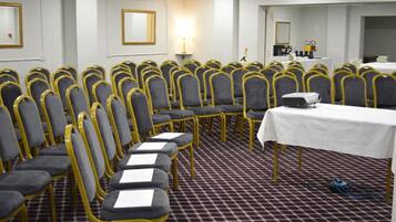 Un salón de conferencias con filas de sillas, una mesa y un proyector.