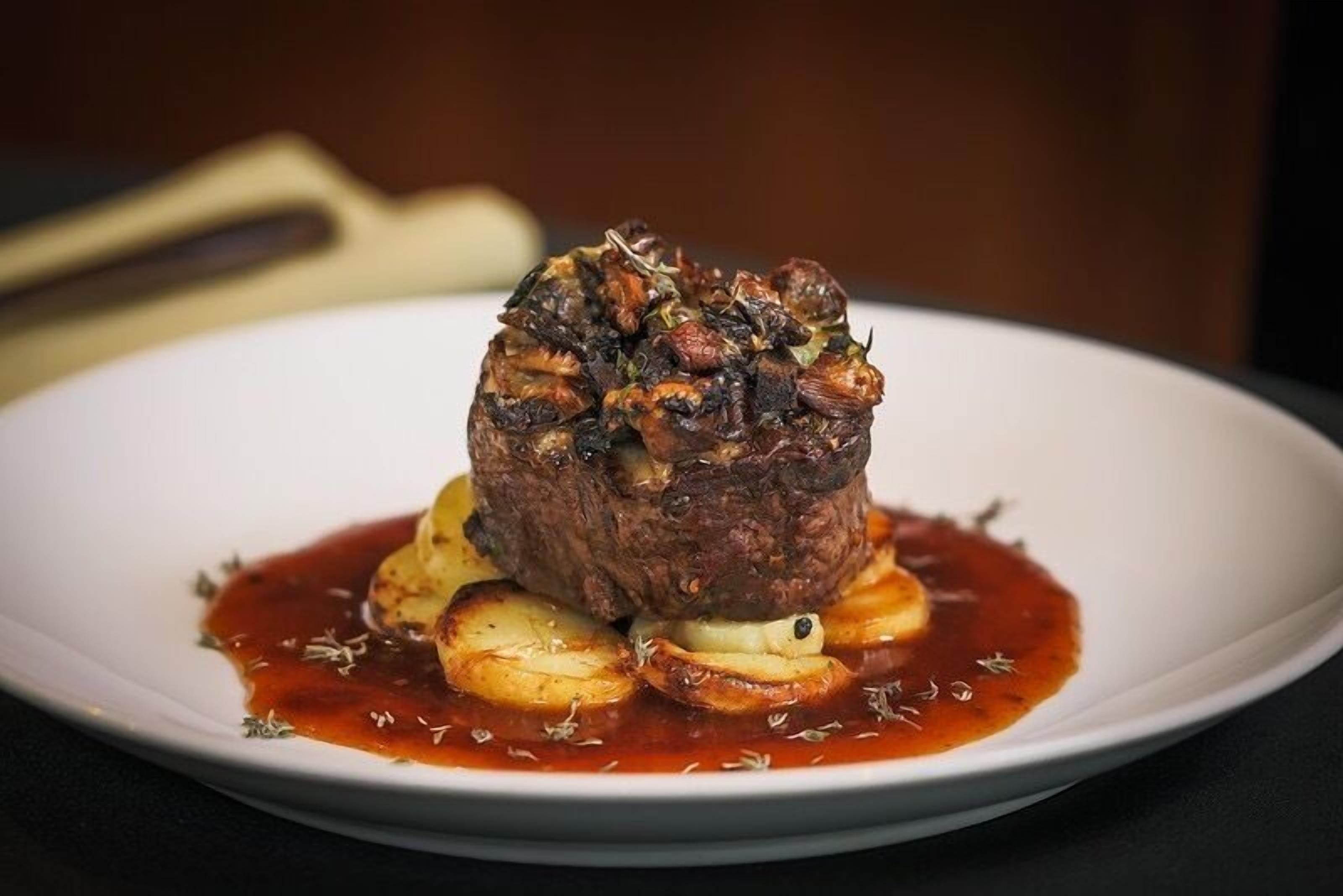 A steak with roasted potatoes and a red sauce on a white plate.