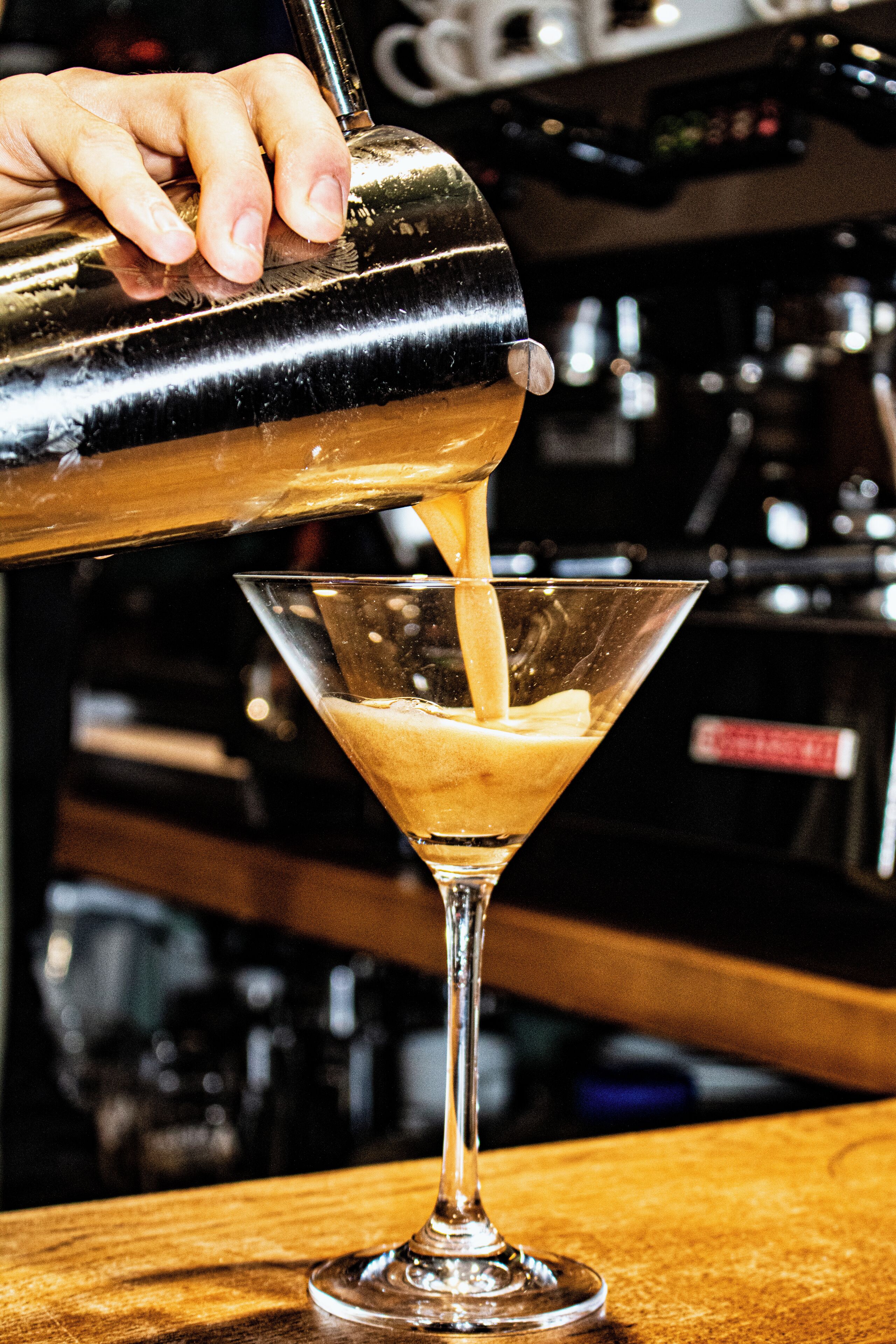 A bartender pouring a drink into a martini glass.