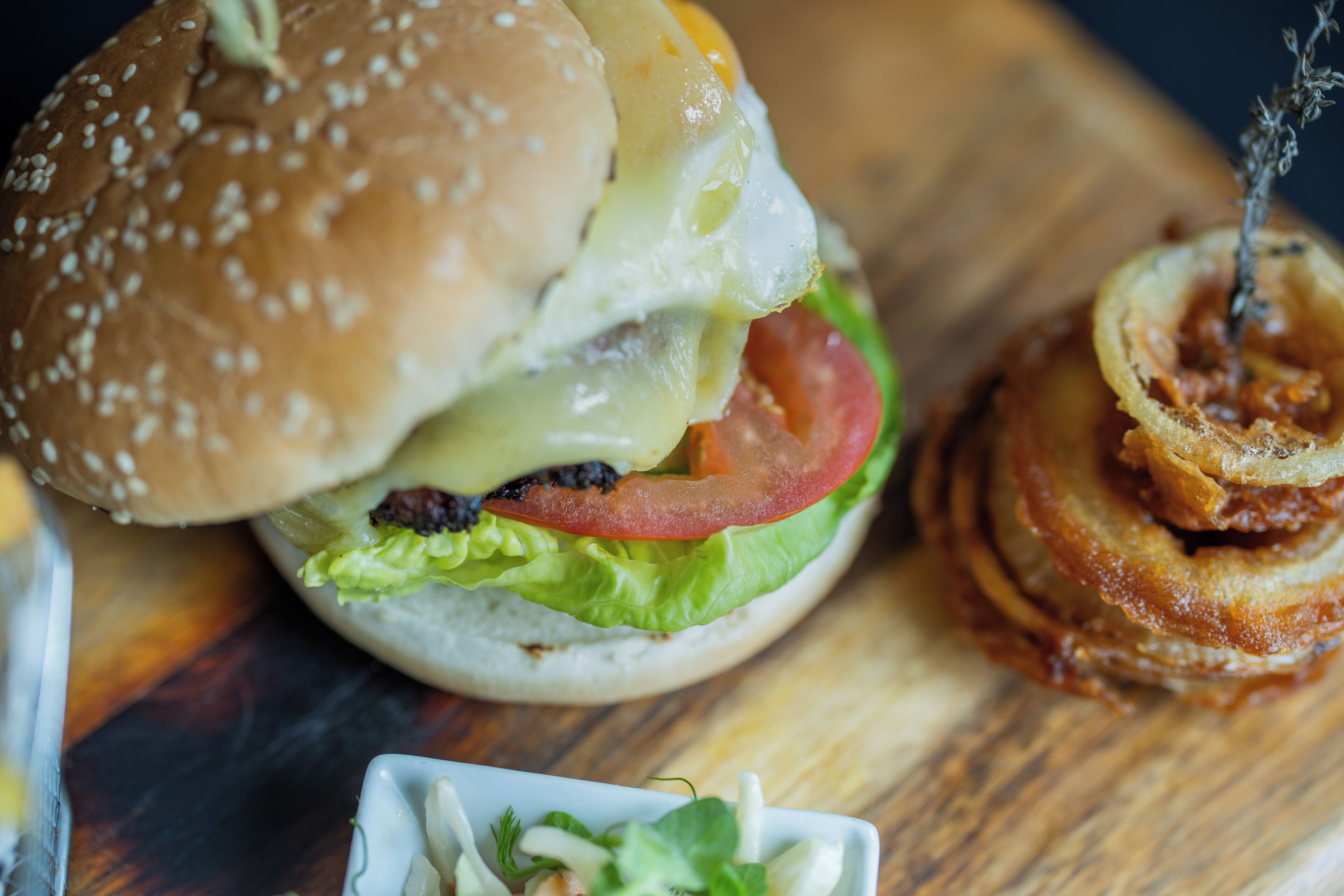 Un hamburger con pane ai semi di sesamo, formaggio, lattuga, pomodoro e una frittura a lato.