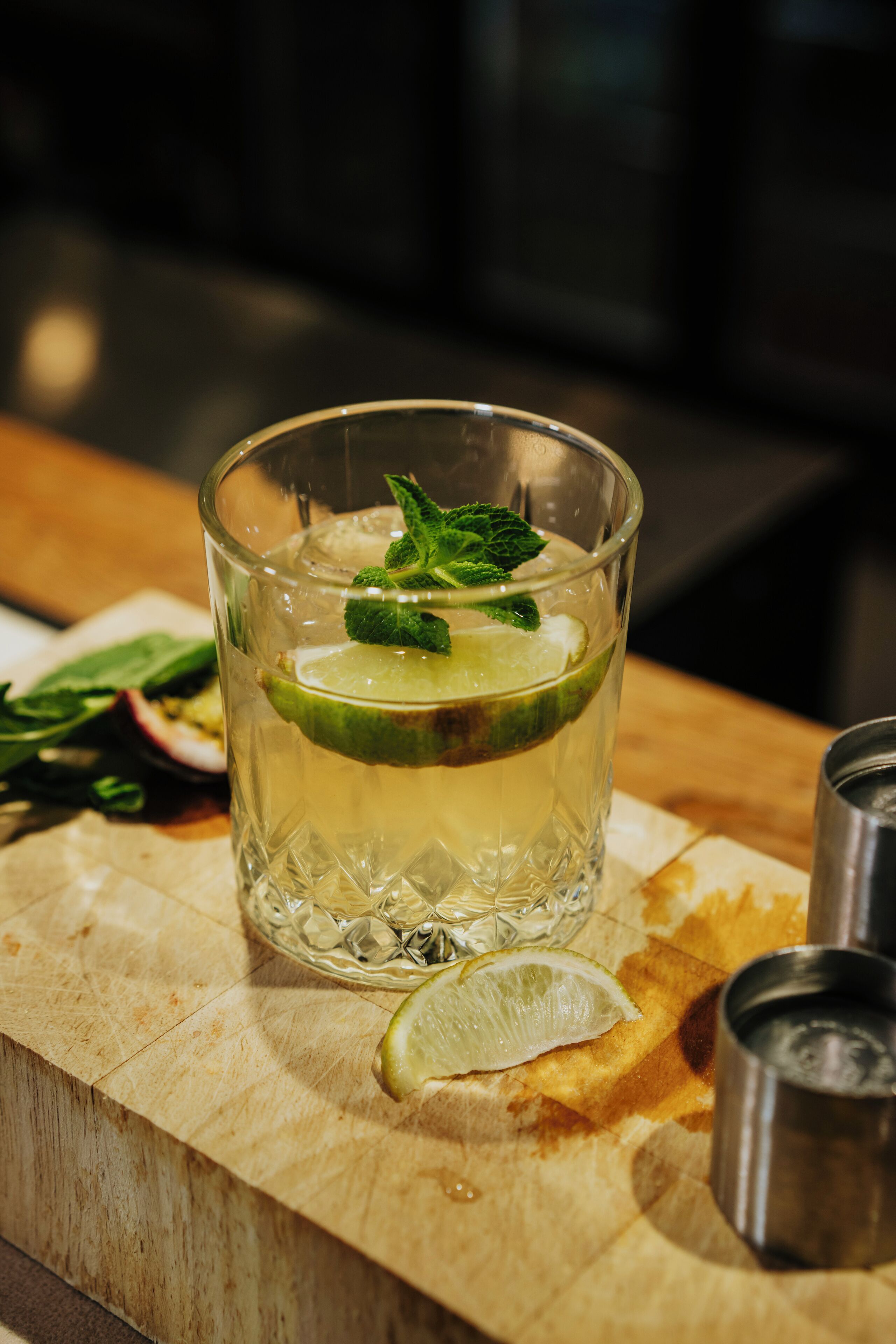 Un vaso de bebida con adorno de lima y menta sobre una superficie de madera.