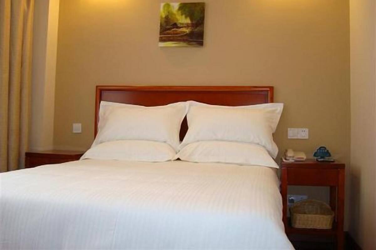 A neatly made bed with white linens, a wooden headboard, and a small bedside table with a lamp and a basket.