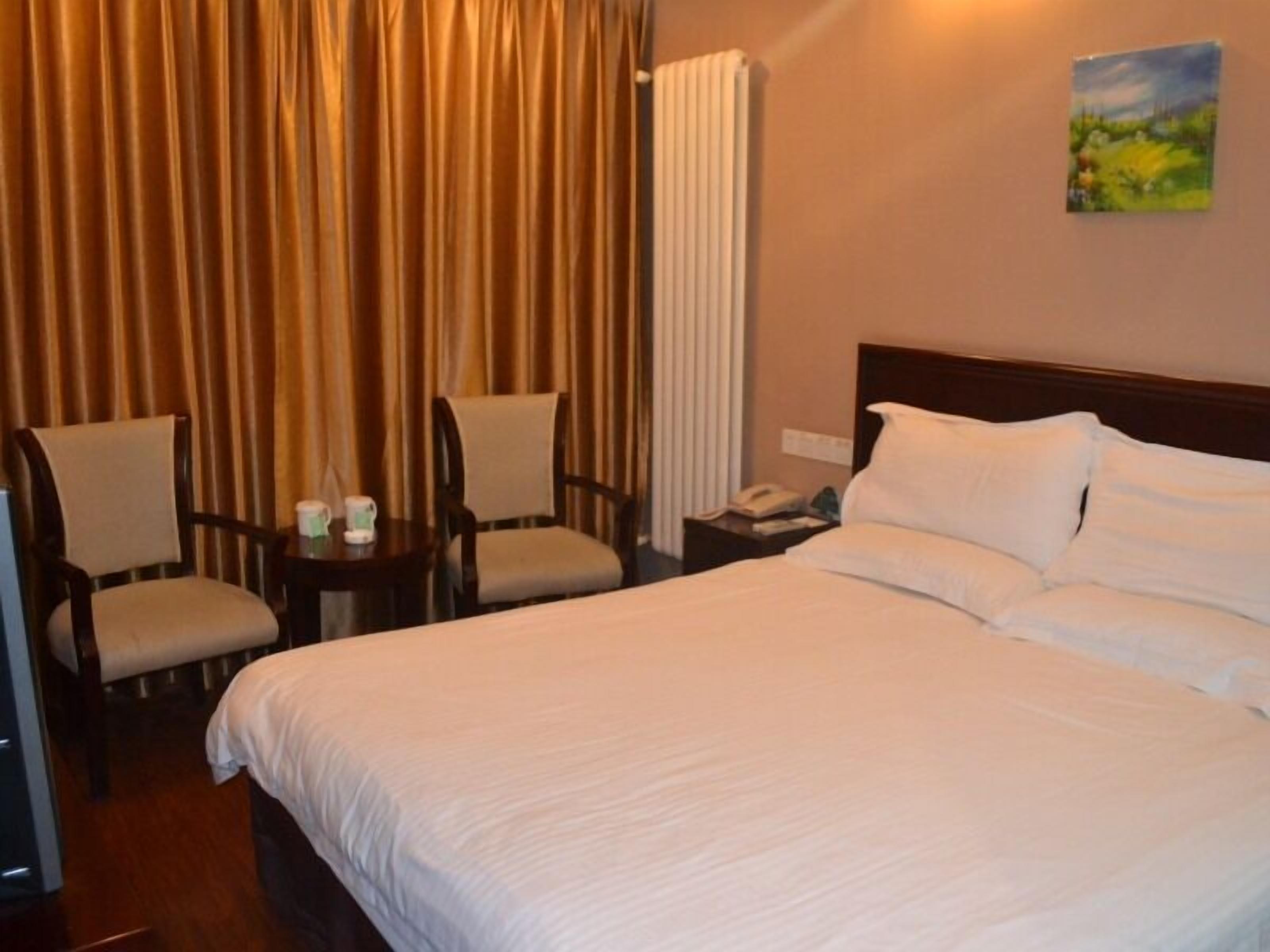 A hotel room with a large bed, two armchairs, a bedside table with a phone, and a painting on the wall.
