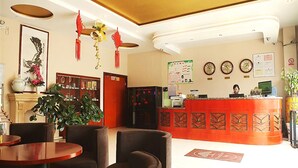 Un vestíbulo de hotel con mostrador de recepción, zona de estar y elementos decorativos como plantas y obras de arte en la pared.