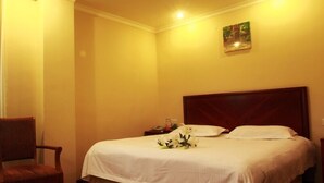 Una habitación de hotel con una cama grande, cabecera de madera, una mesita de noche con lámpara y una silla.