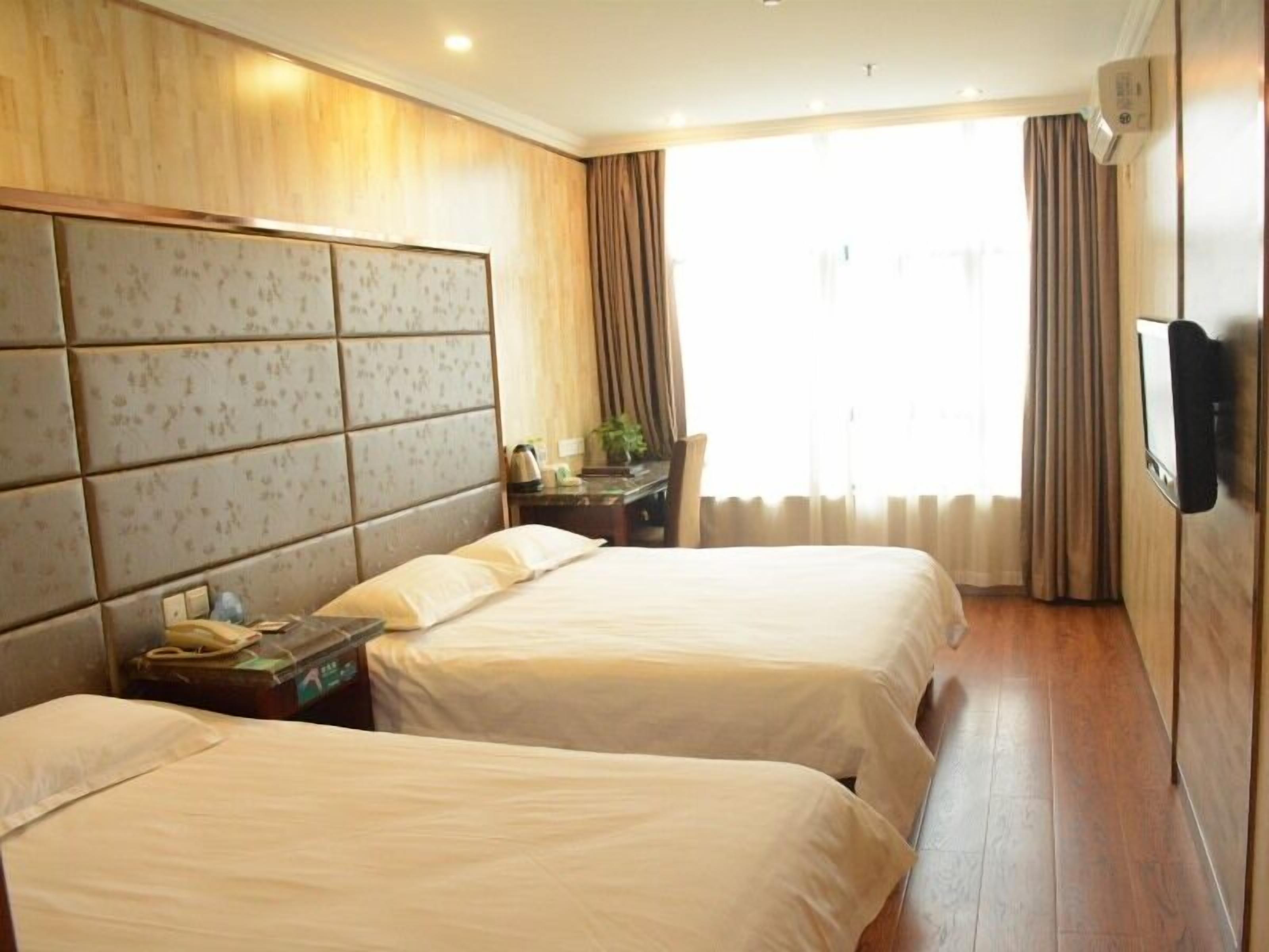 A hotel room with two beds, a wooden headboard, a flat-screen TV, and a large window with curtains.