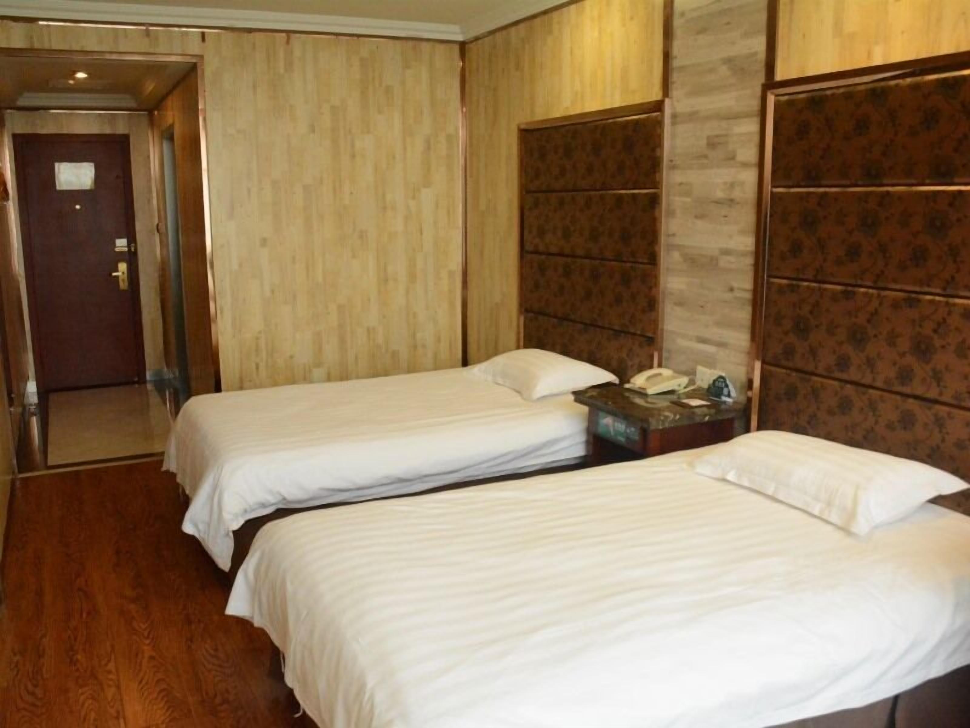 A hotel room with two single beds, a wooden headboard, a bedside table with a phone, and a door leading to another room.