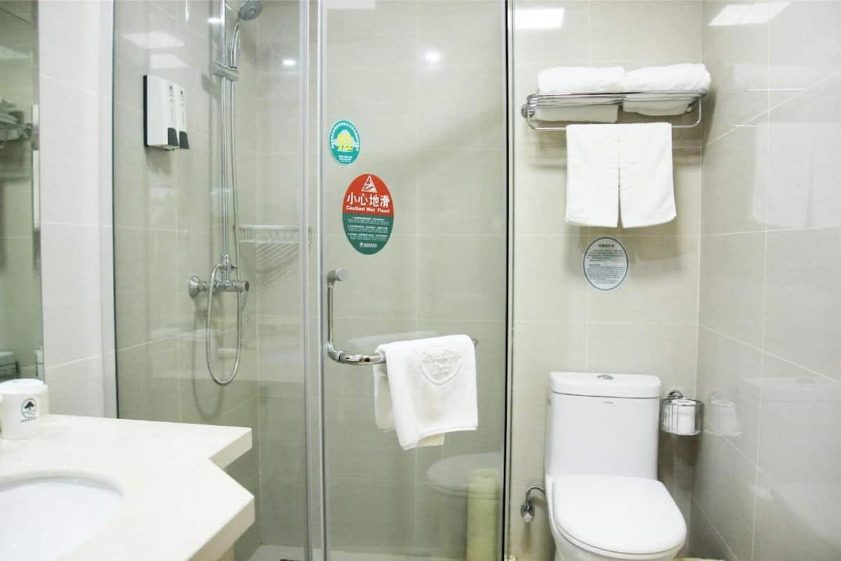 A bathroom with a glass shower enclosure, a toilet, and a sink. There are towels hanging on a rack and a soap dispenser on the wall.