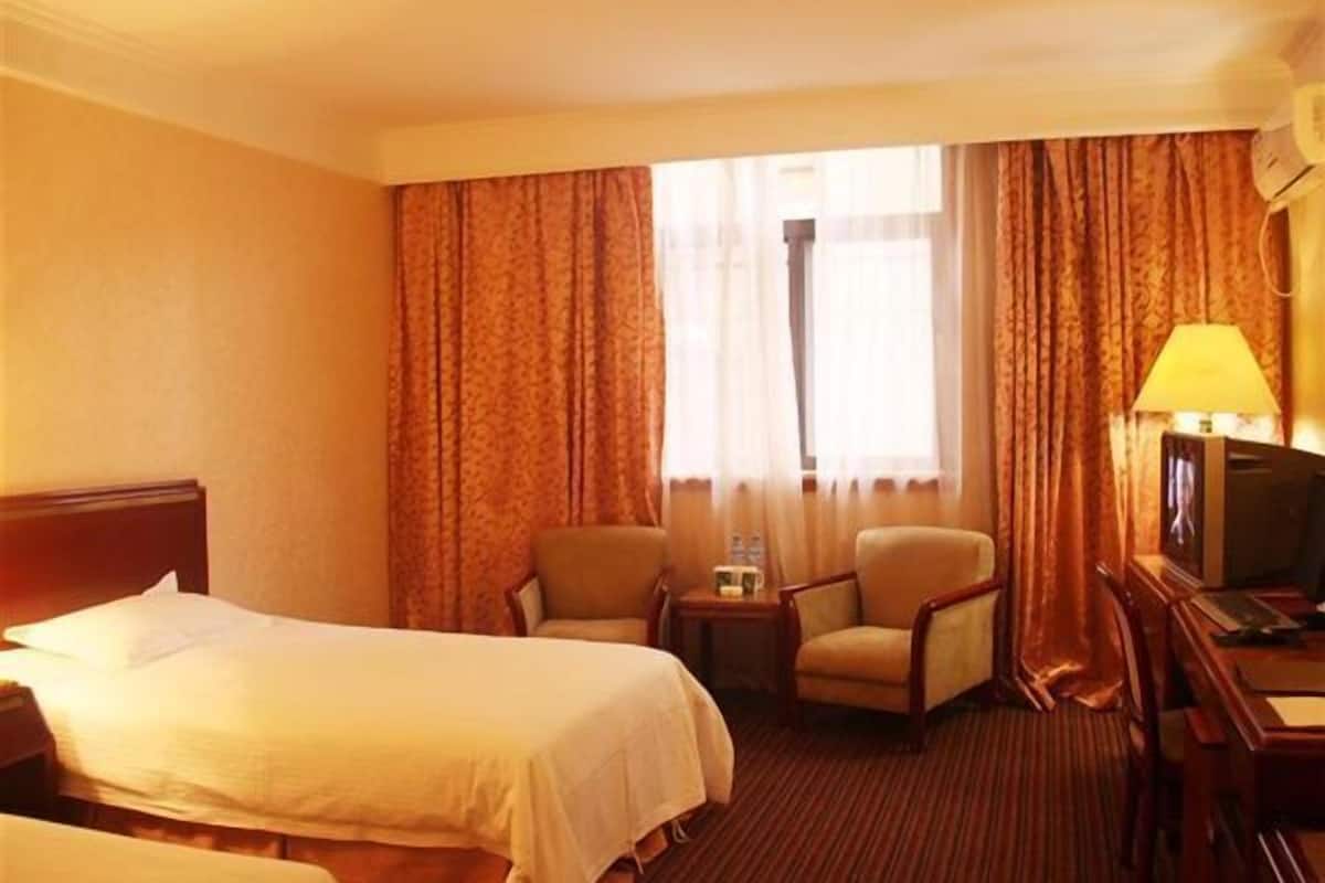 A hotel room with two beds, a TV, a chair, and a small table with a lamp.