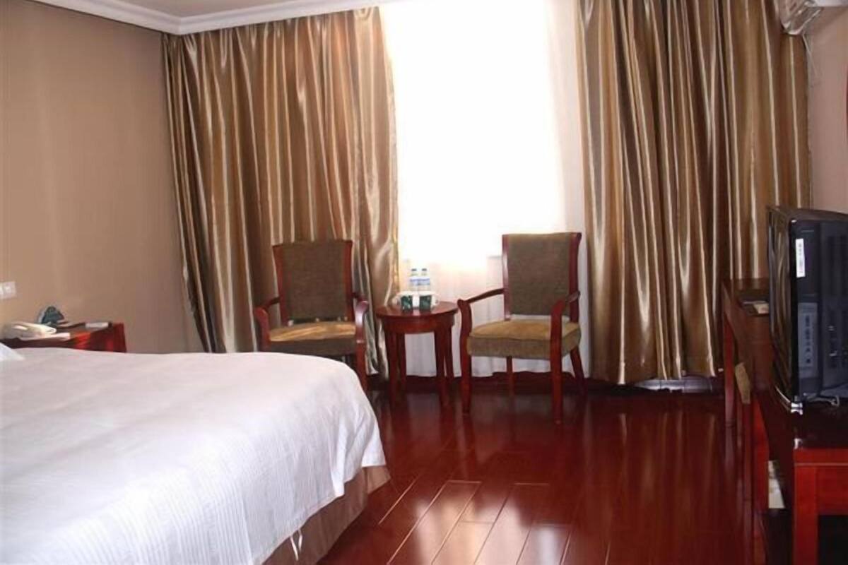 A hotel room with a large bed, two armchairs, a small table, and a television.