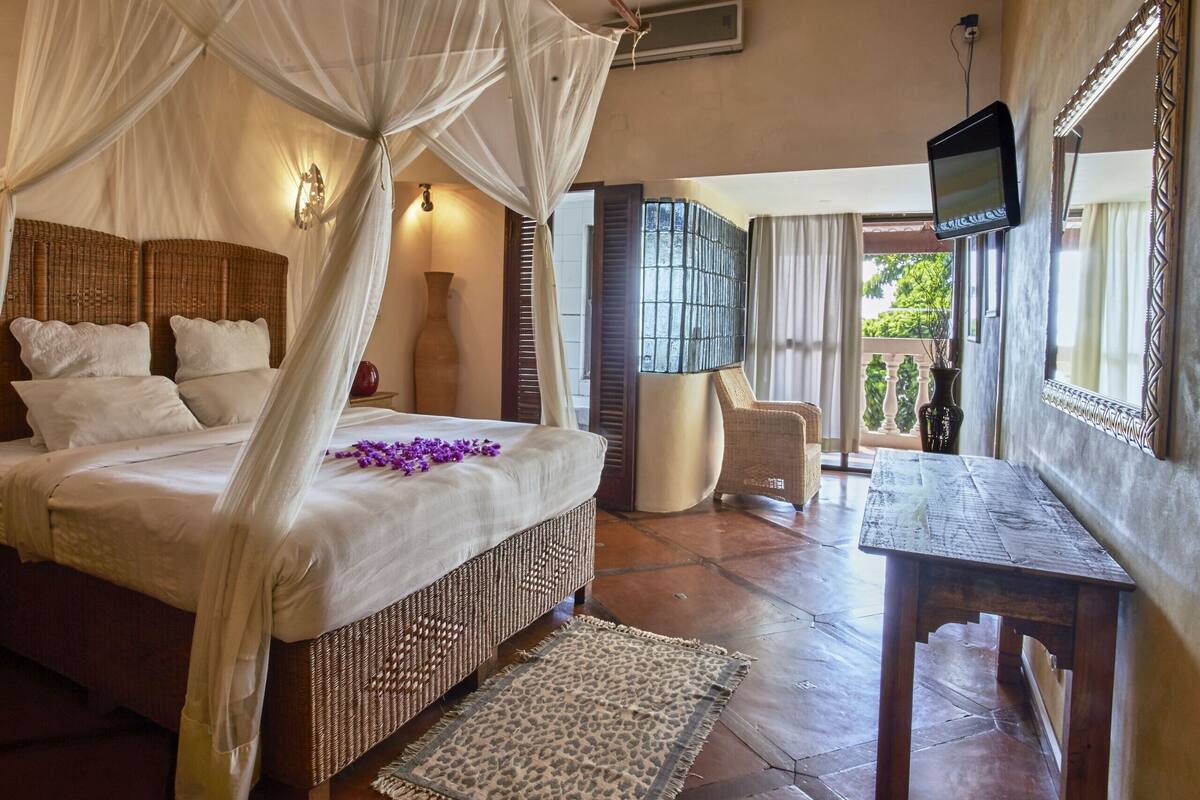 A bedroom with a canopy bed, a television, and a view of the outdoors.
