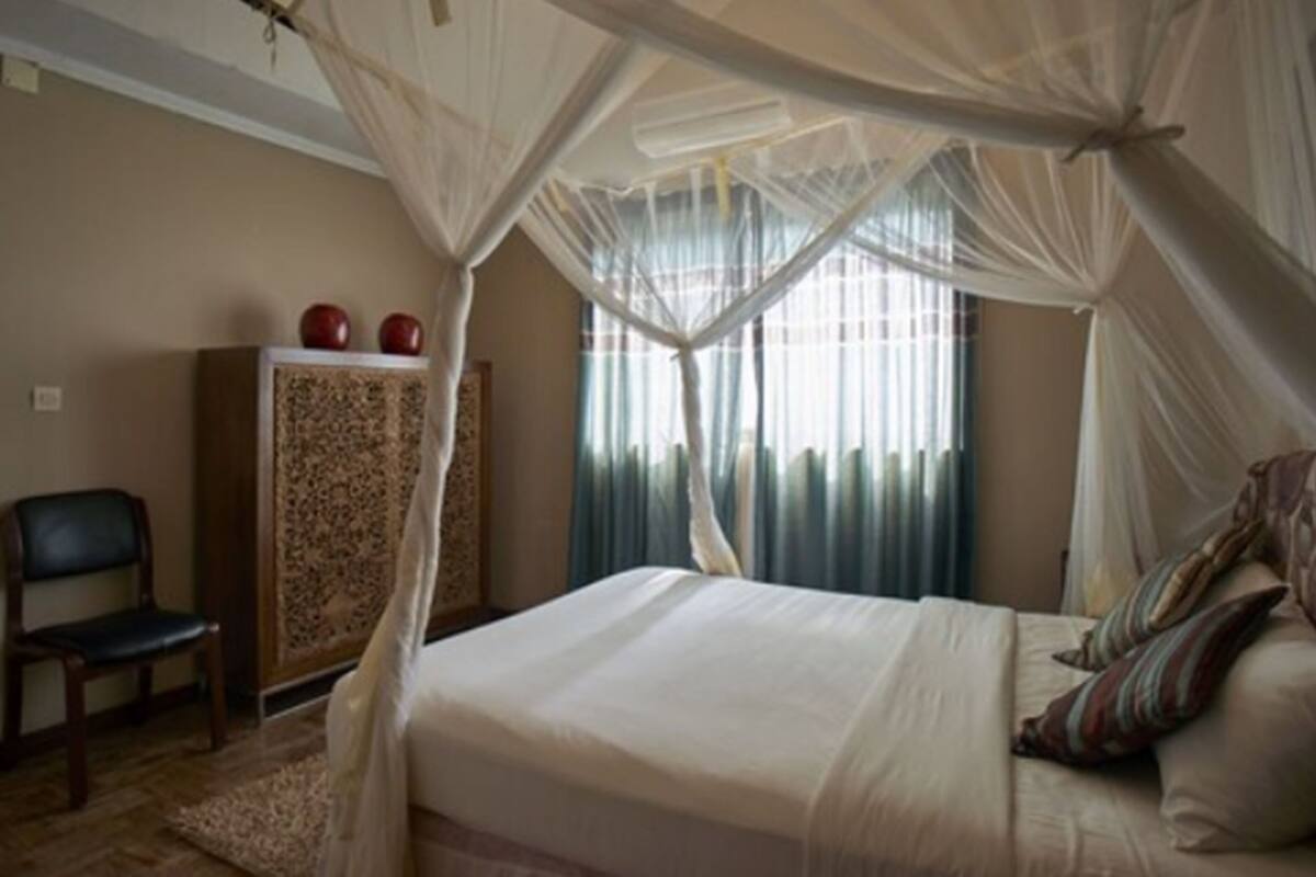 A bedroom with a canopy bed, a chair, and a cabinet.