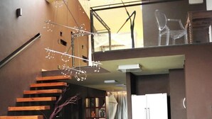 A modern interior with a wooden staircase, a glass railing, and a high ceiling with a skylight. - Catembe Gallery Hotel (Maputo)