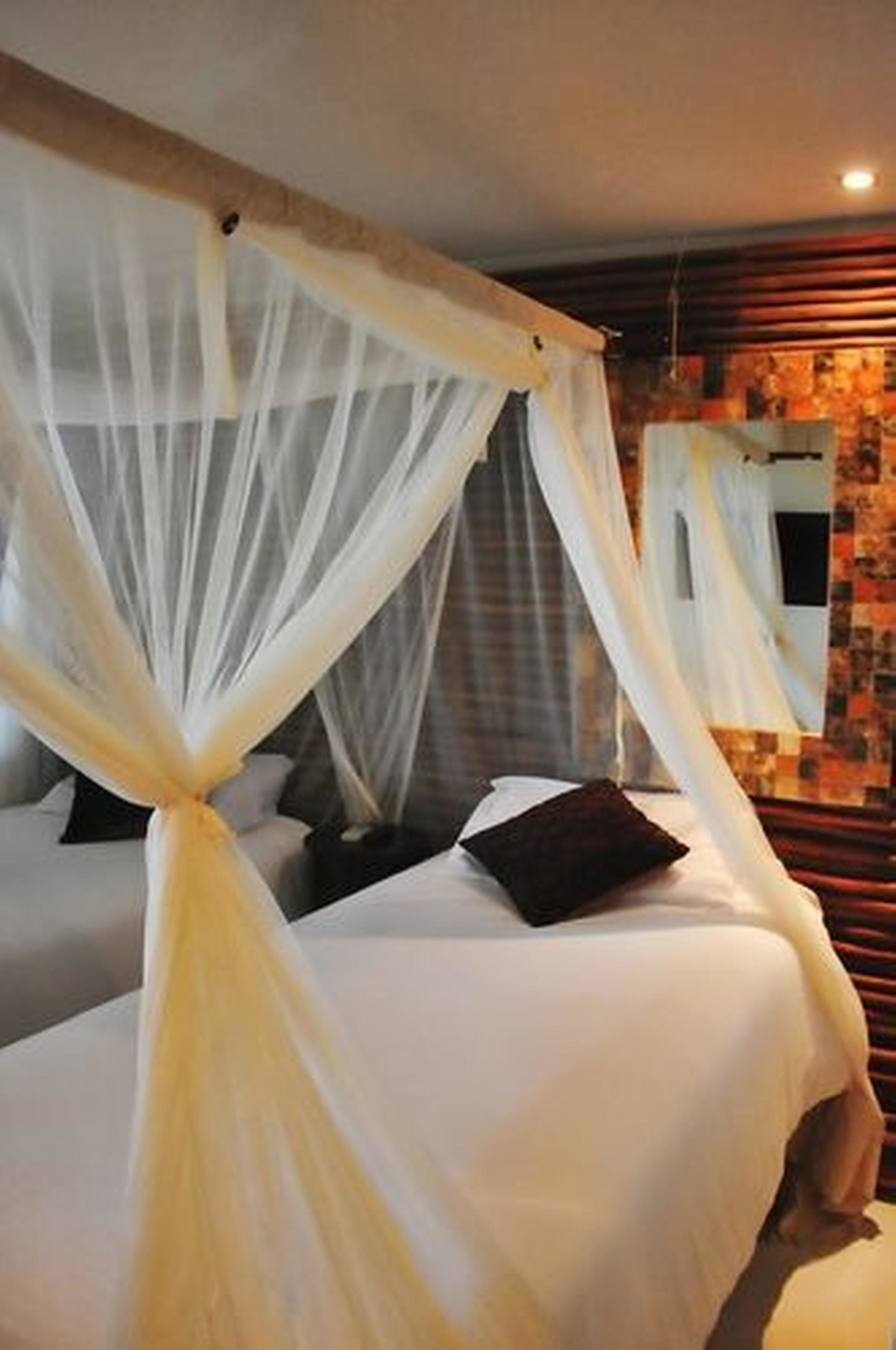 A bed with a canopy and a headboard, a wall with a patterned design, and a mirror.