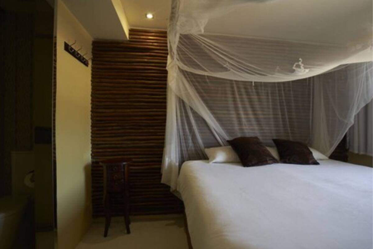 A bedroom with a bed under a mosquito net, a chair, and a staircase with wooden steps.