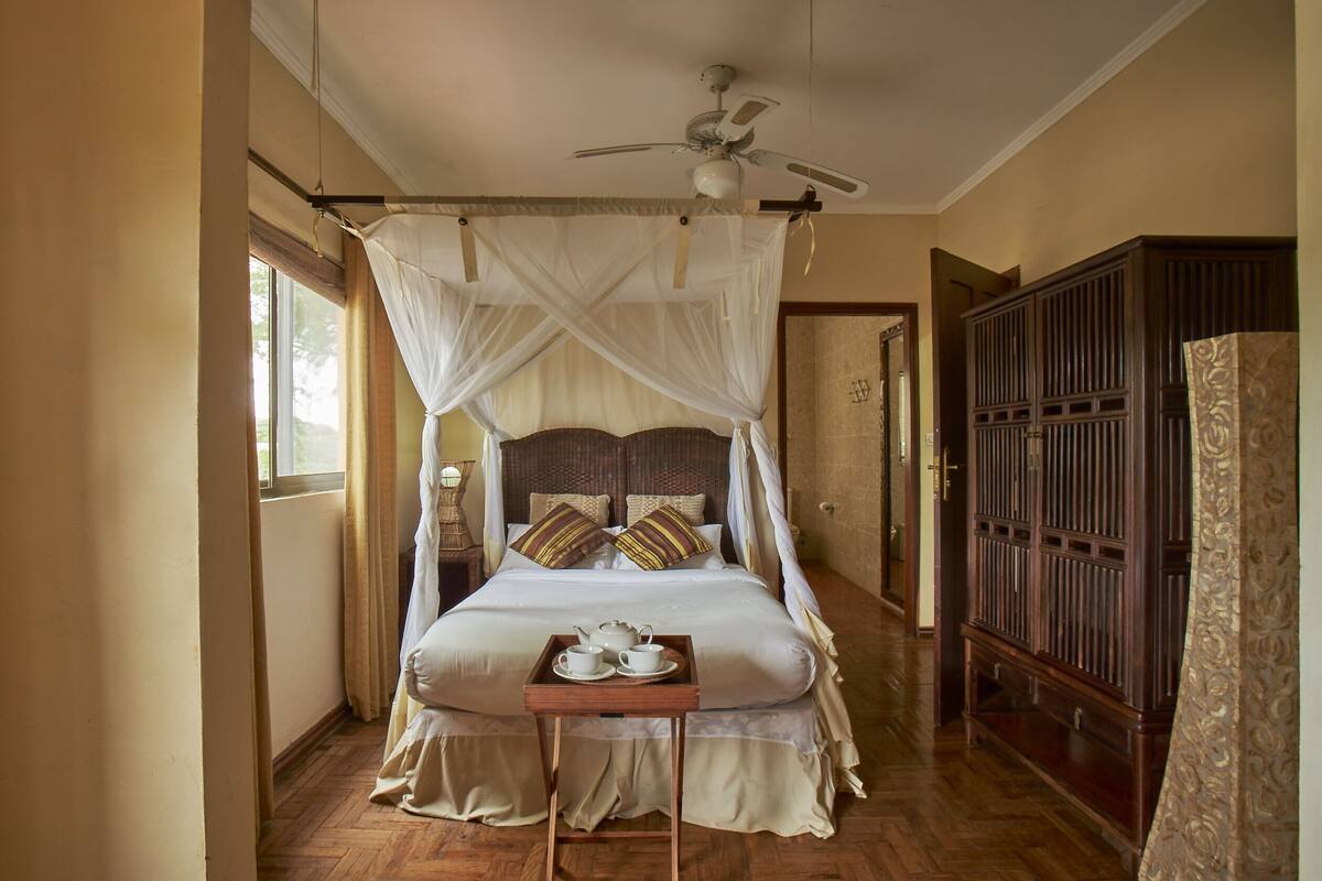 A bedroom with a four-poster bed, a bedside table with a tray of tea, and a wooden wardrobe.