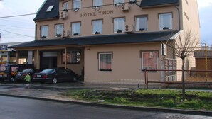 A two-story building with a sign reading "HOTEL TION." It has multiple windows, a flat roof, and a parking area in front. - Timon (Budapest)