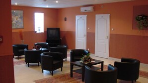 A hotel room with a TV, multiple black armchairs, a coffee table, and a patterned rug. - Timon (Budapest)