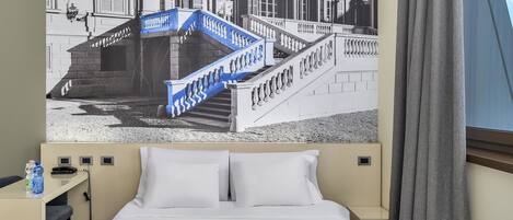 A hotel room with a bed, a nightstand, a lamp, and a view of a building with a blue staircase.