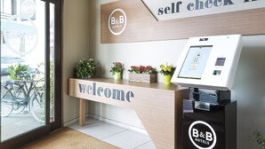 Una recepción con un cartel de 'Welcome', un quiosco de registro automático y un cartel para 'B&B Hotels'.