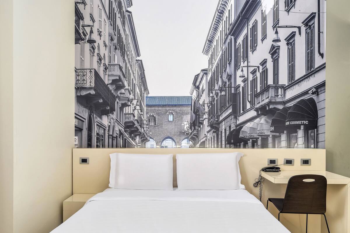 A hotel room with a large bed, a desk, and a chair.