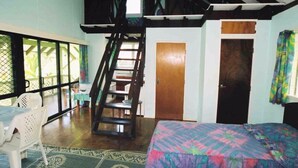 A room with a bed, a staircase, a small table, and a chair. - Gina's Garden Lodges (Aitutaki)