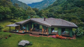 A two-story house with a covered porch and a deck, surrounded by lush greenery and mountains. - El Silencio Lodge and Spa (Toro Amarillo)