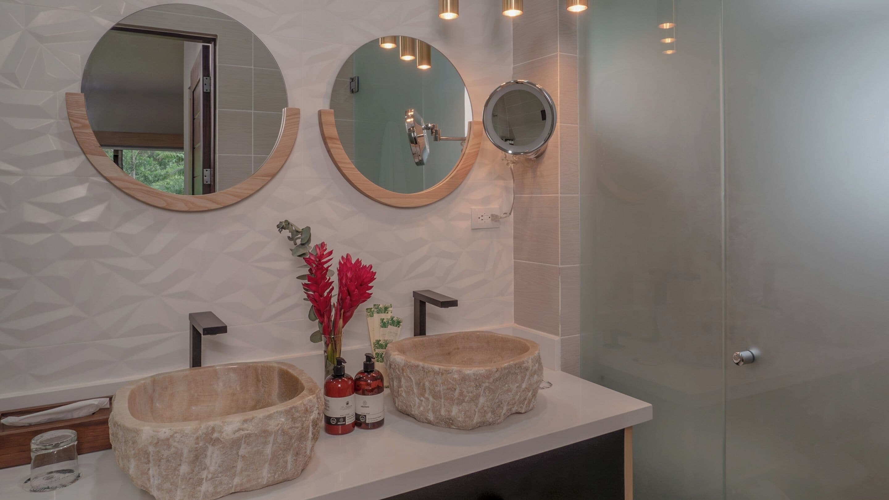 A bathroom with two stone sinks, a mirror, and a vase with red flowers.