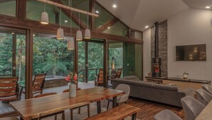 A spacious living area with a wooden dining table, comfortable seating, a fireplace, and large windows offering a view of the outdoors. - El Silencio Lodge and Spa (Toro Amarillo)