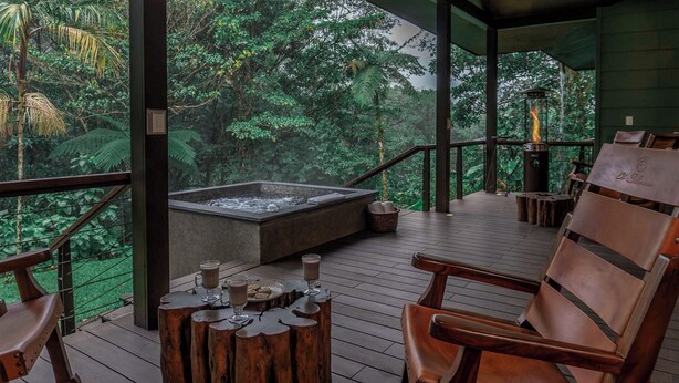 A wooden deck with a hot tub, wooden chairs, and a view of lush greenery. - El Silencio Lodge and Spa (Toro Amarillo)