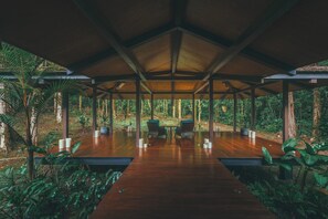 A covered wooden deck with a central table and chairs, surrounded by lush greenery. - El Silencio Lodge and Spa (Toro Amarillo)