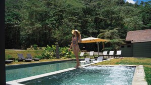 A swimming pool with a person standing on the edge, surrounded by lounge chairs and greenery. - El Silencio Lodge and Spa (Toro Amarillo)