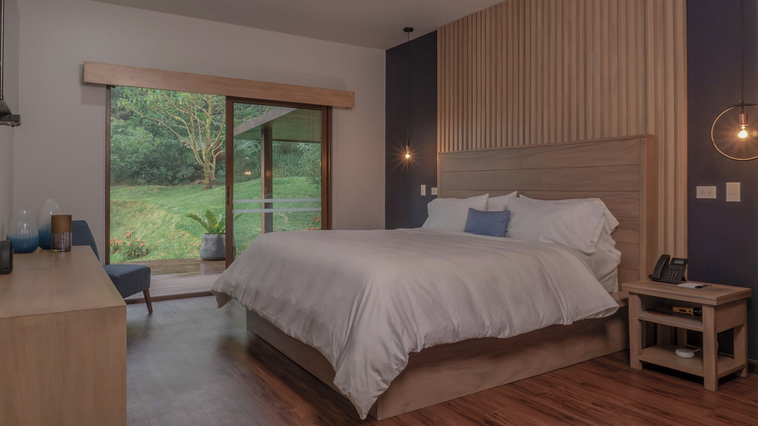 Un dormitorio moderno con una cama grande, un escritorio y vistas a un jardín a través de una puerta corredera.
