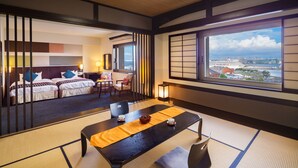 A traditional Japanese-style hotel room with tatami flooring, a low table with a yellow mat, and a view of a port with ships and cranes. - Navios Yokohama (Yokohama)