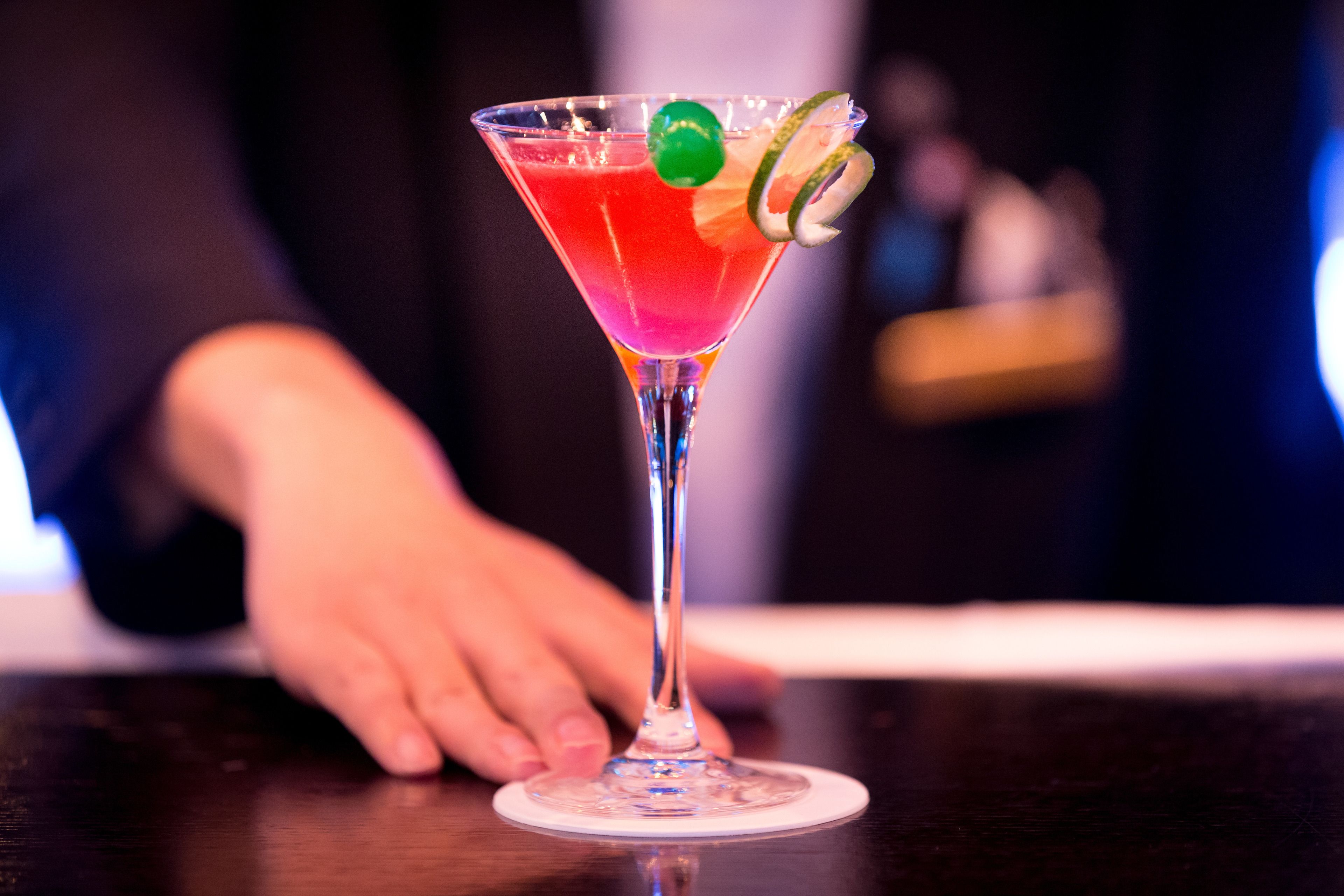 Een martini glas met een limoenpartje en een groene garnering op een bar.