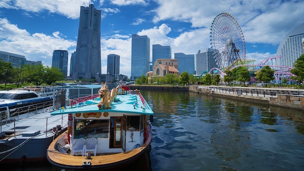 A river with a boat docked, a Ferris wheel, and modern skyscrapers in the background. - Navios Yokohama (Yokohama)