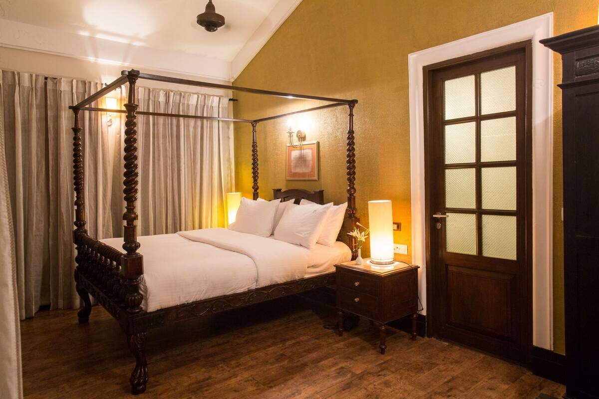 A four-poster bed with a wooden frame and white bedding, a nightstand with a lamp, and a door with glass panels.
