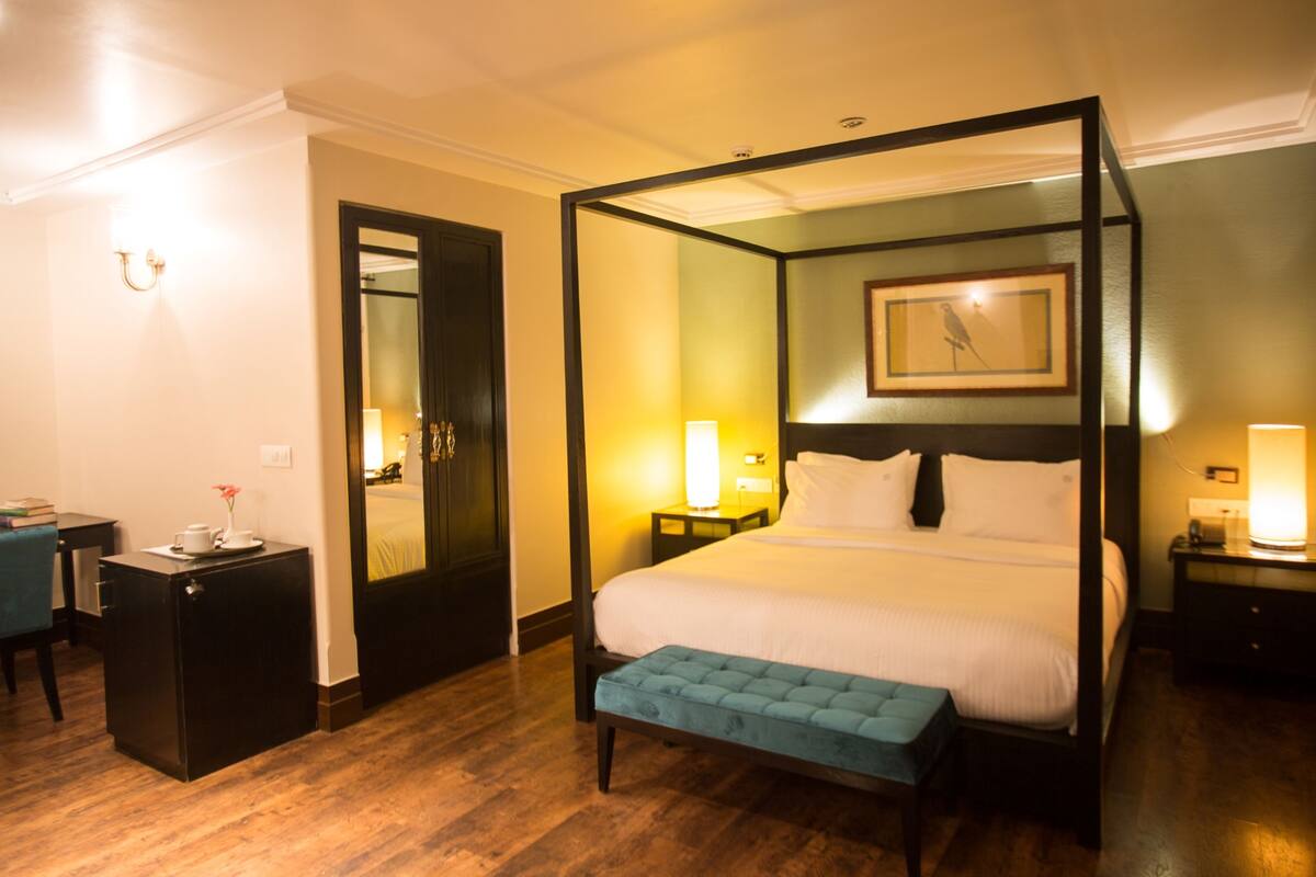 A four-poster bed with a bench, bedside tables, a desk, and a framed picture on the wall.