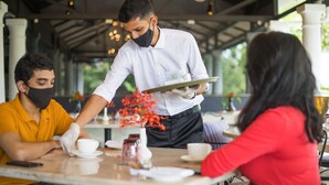 A waiter serving coffee to guests at a table in a covered outdoor cafe with a modern design and natural lighting. - Sol De Goa by Sereno (Nerul)