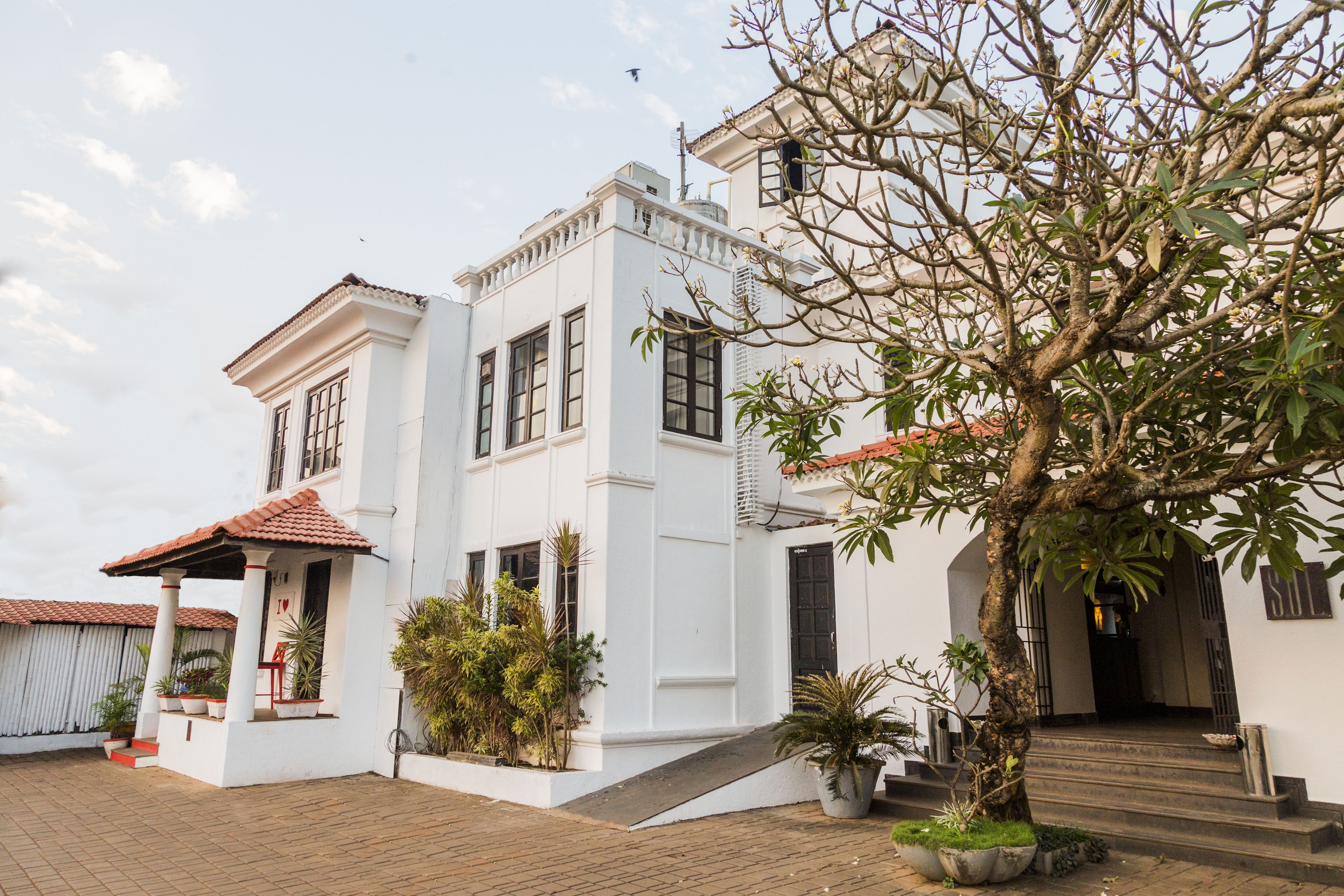 A white building with a red-tiled roof, a covered porch, and a staircase leading to the entrance.
