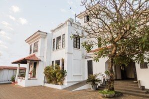 A white building with a red-tiled roof, a covered porch, and a staircase leading to the entrance. - Sol De Goa by Sereno (Nerul)