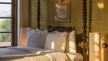 A four-poster bed with a wooden frame, a bedside table with a lamp, and a window with a view of greenery.