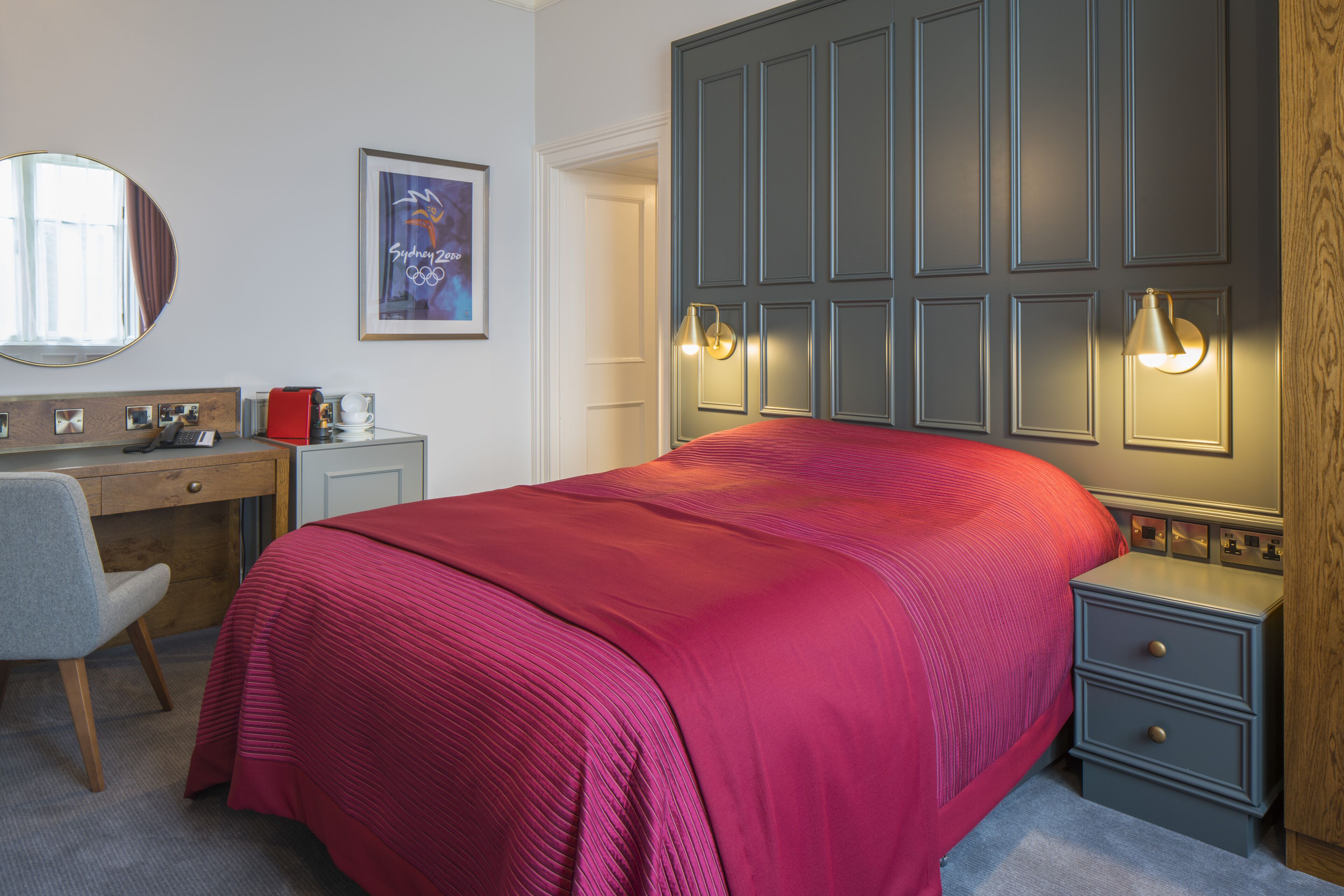 Ein Hotelzimmer mit einem großen Bett, einem Schreibtisch mit Stuhl, einem Nachttisch und einem Kleiderschrank.