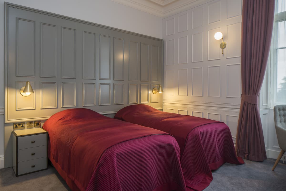 A bedroom with two beds, a nightstand, a chair, and a window with curtains.