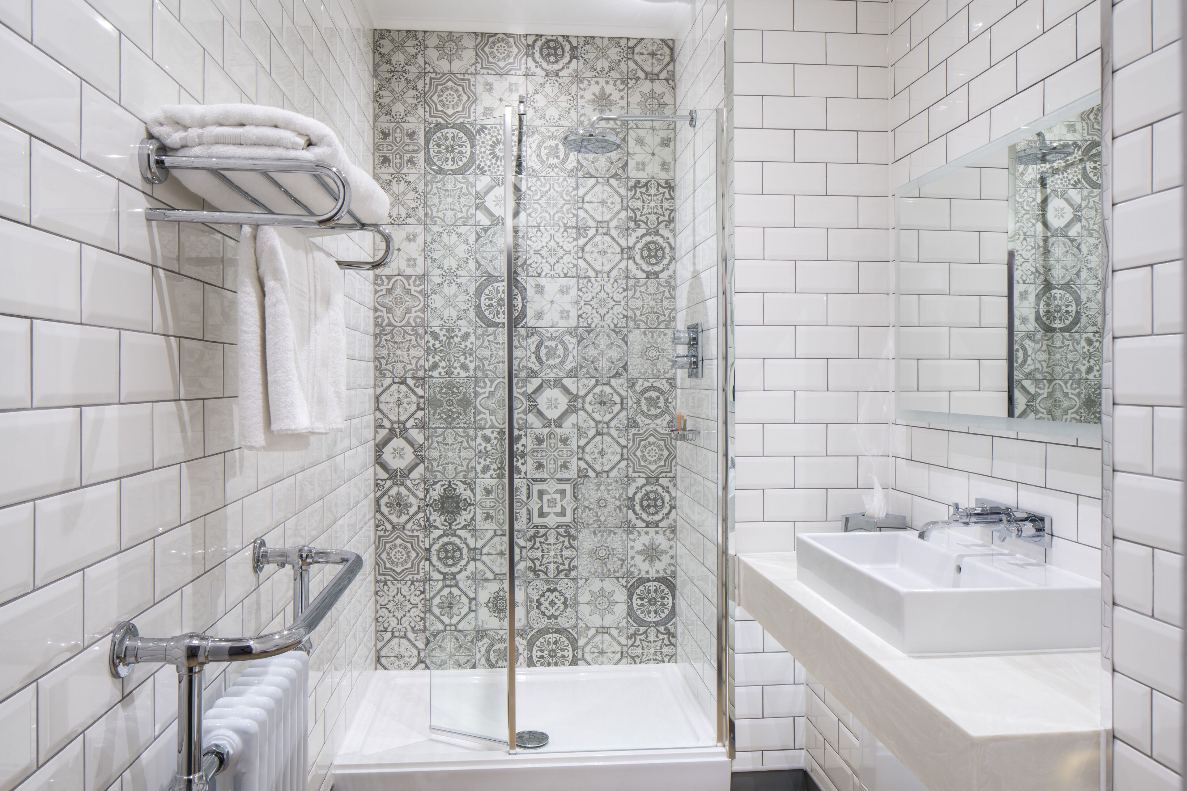 A bathroom with a shower, a sink, a towel rack, and patterned tiles.