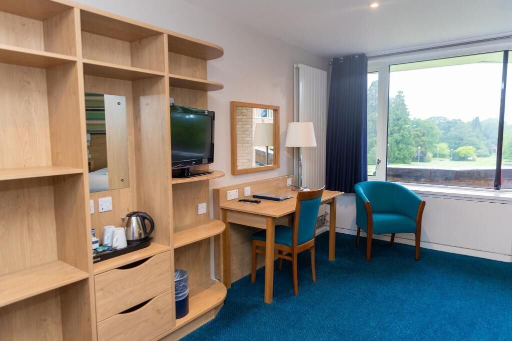 Une chambre d’hôtel avec un bureau en bois, une télévision, un miroir, une lampe et une fenêtre donnant sur un paysage verdoyant.